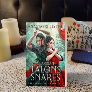 The mockup cover of Guardians of Talons and Snares with candles, a Kindle and a plush background